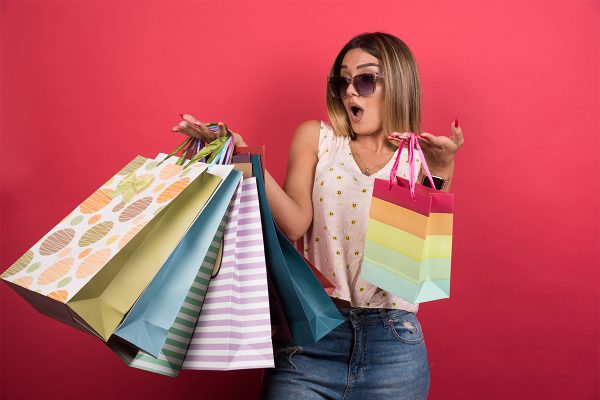 Woman carrying shopping bags with surprised expression on red background . High quality photo
